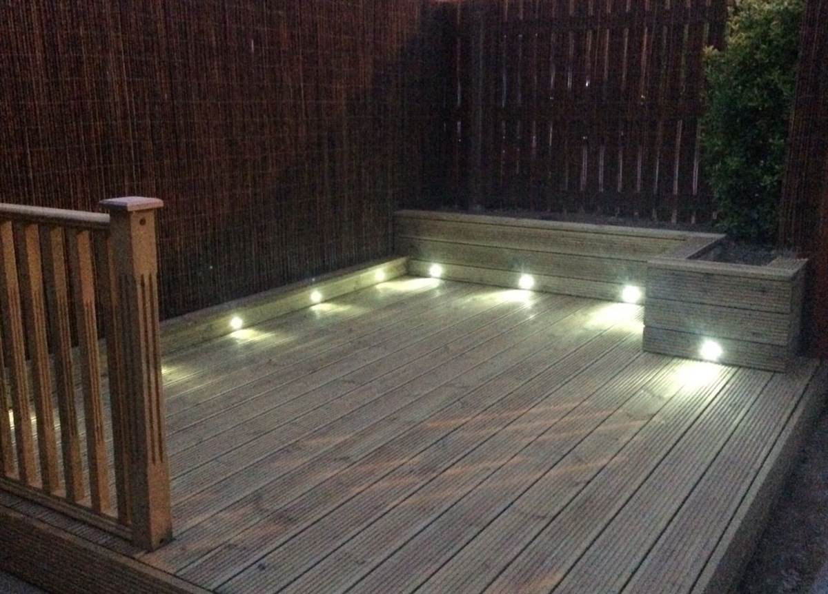 After — deck lit up at night with recessed deck lights in the steps and planters